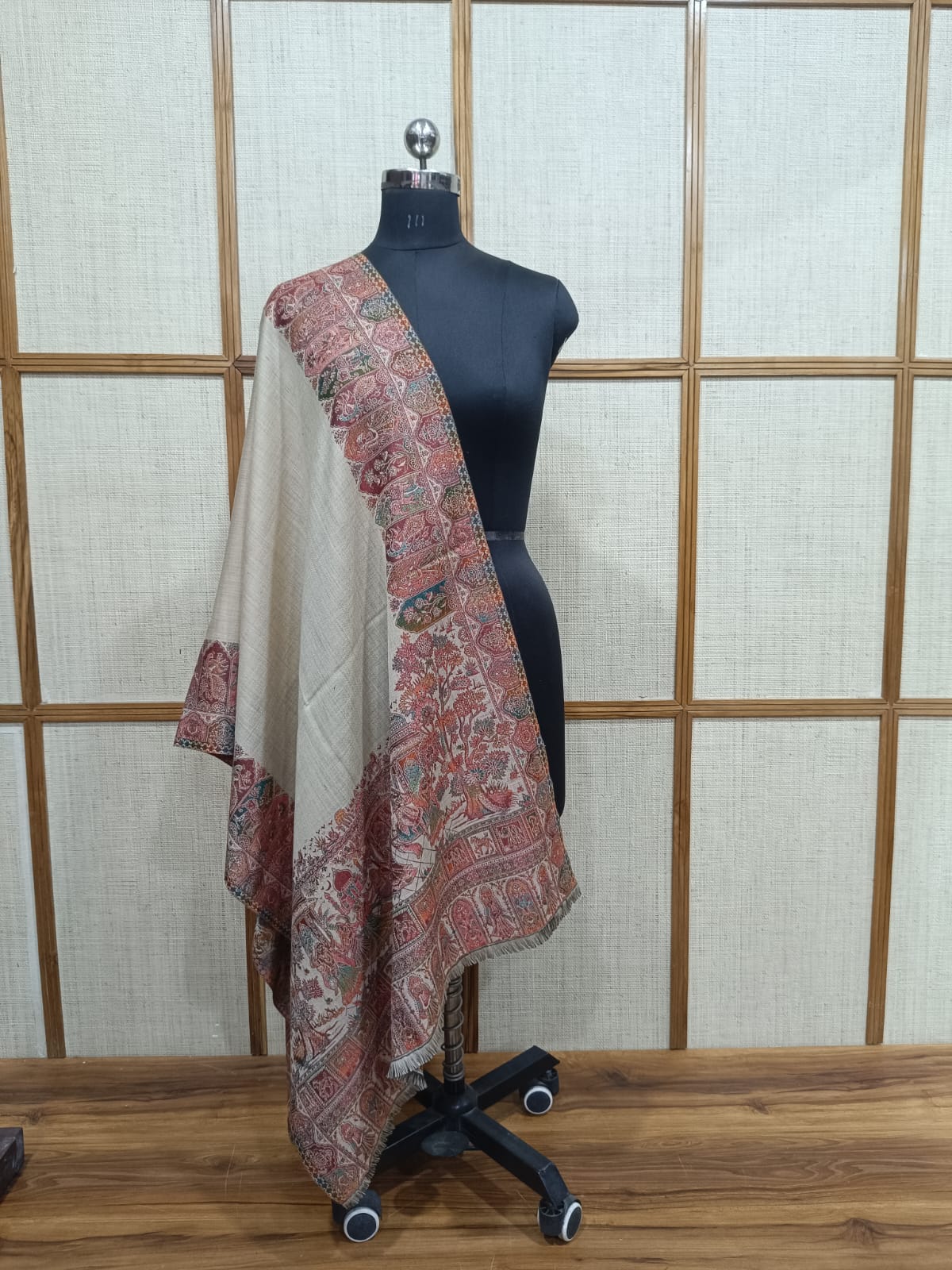 Mannequin wearing a patterned shawl against a wooden panel background