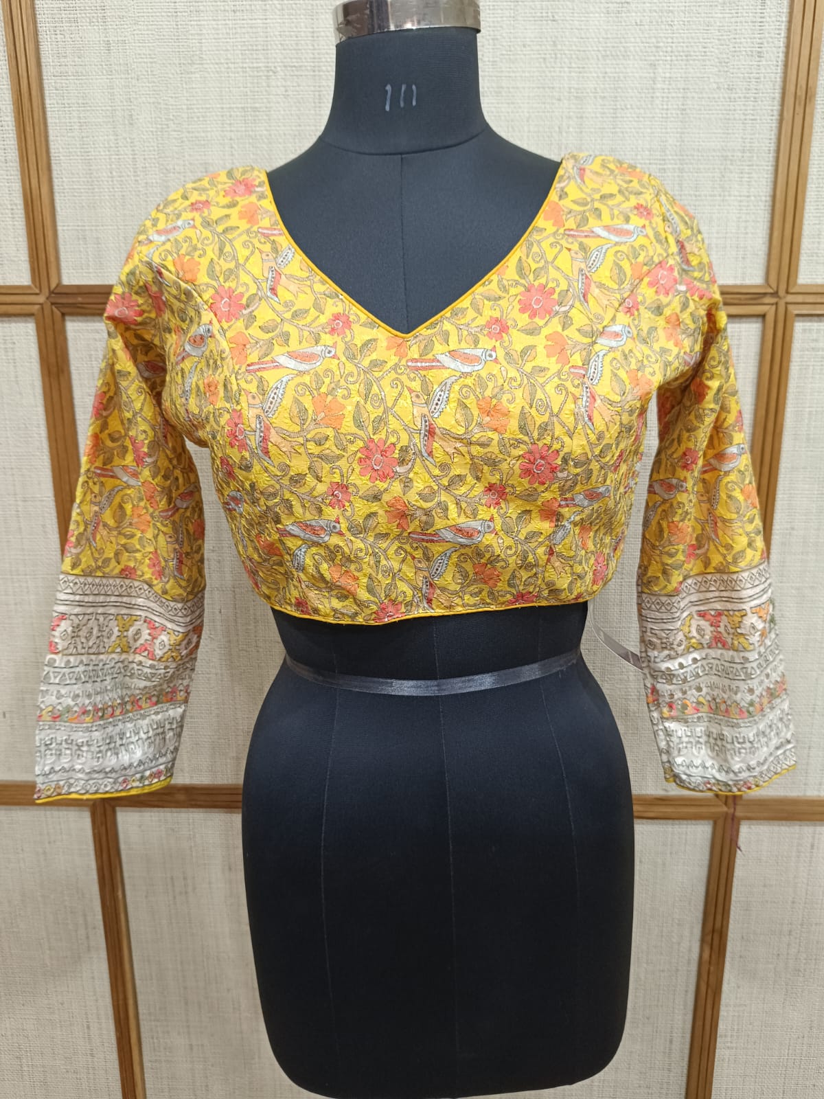 Yellow floral blouse with long sleeves on a mannequin against a textured wall.
